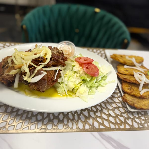 Fried pork with onions, a side salad, and fried plantains on a white plate and platter.