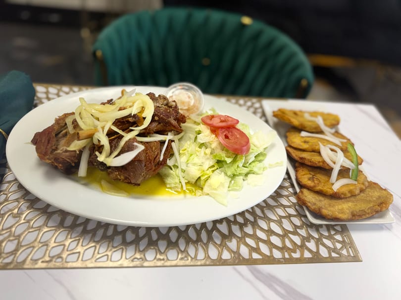 Fried pork with onions, a side salad, and fried plantains on a white plate and platter.