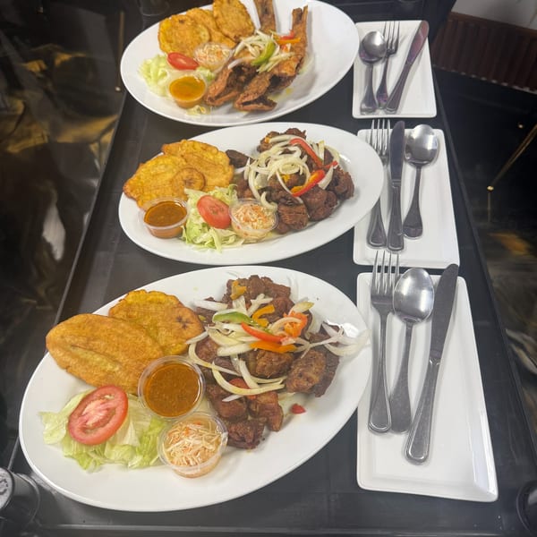 Three plates of Haitian food with fried plantains, meat, salad, and sauces on a serving cart.