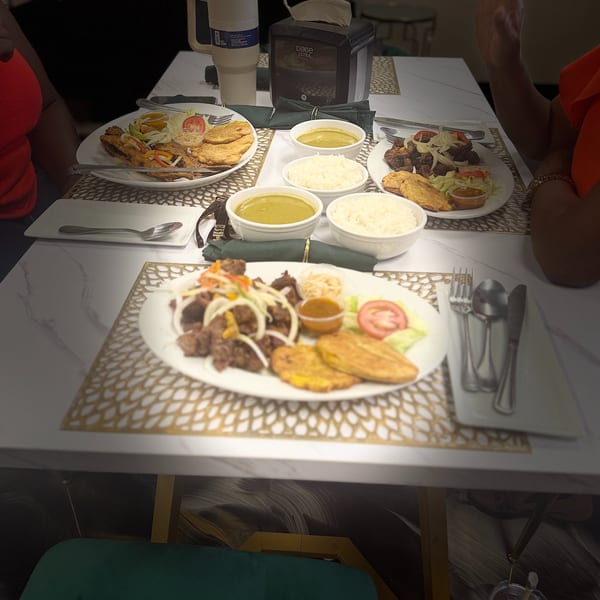 Three plates of food with meat, plantains, rice, and soup on a white marble table.