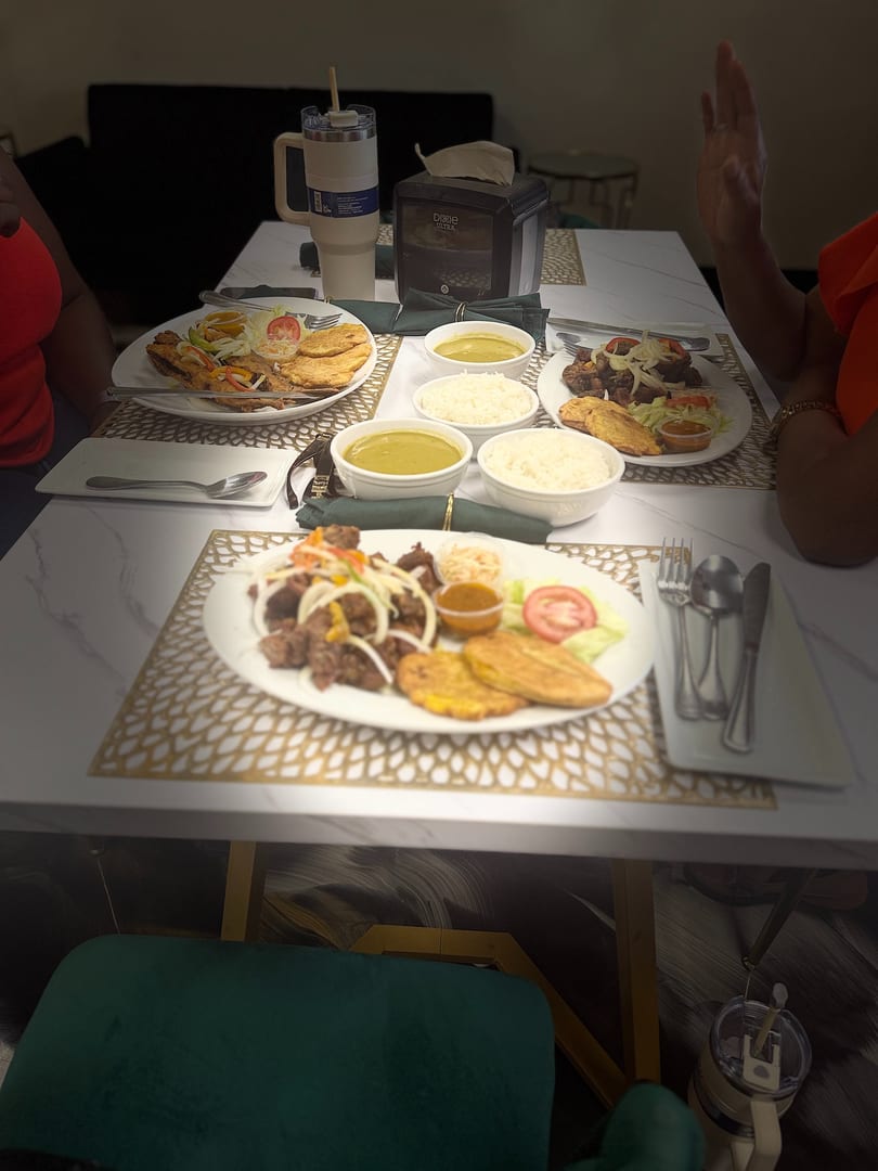 Three plates of food with meat, plantains, rice, and soup on a white marble table.