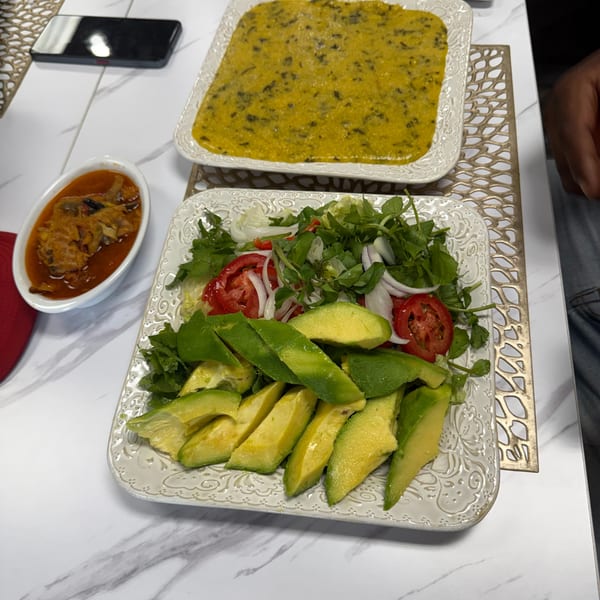 A table set with a vibrant green salad, sliced avocado, a yellow dish, and a bowl of stew.